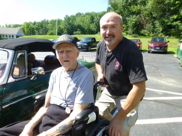 Don Giguere standing beside a veteran using a wheelchair during an outdoor outing